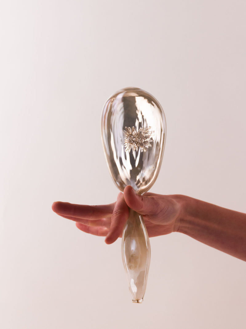 Hand holding a glass object with a flower inside 