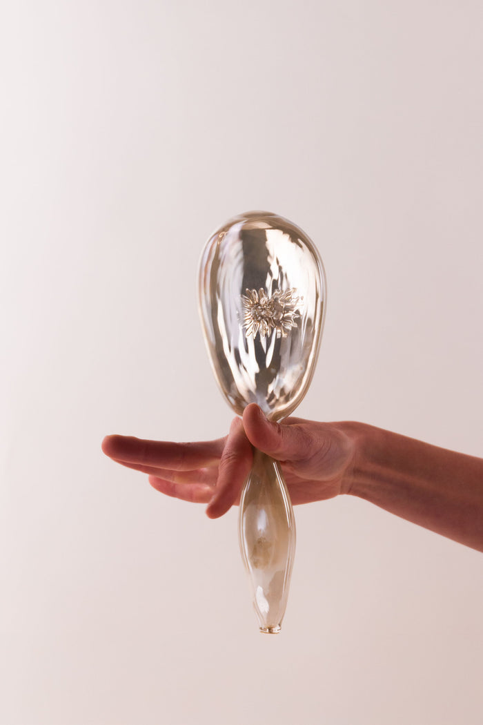 Hand holding a glass object with a flower inside 