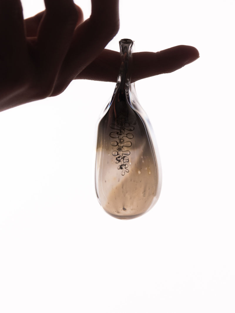 Hand holding a small glass object with bubbles again a bright white background