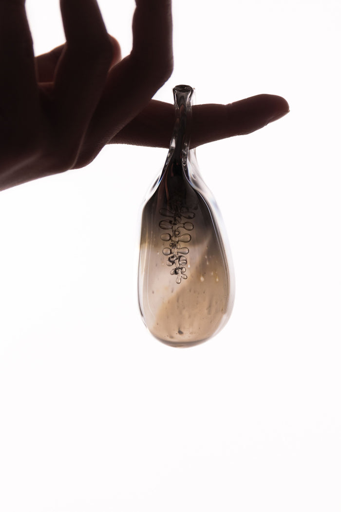 Hand holding a small glass object with bubbles again a bright white background