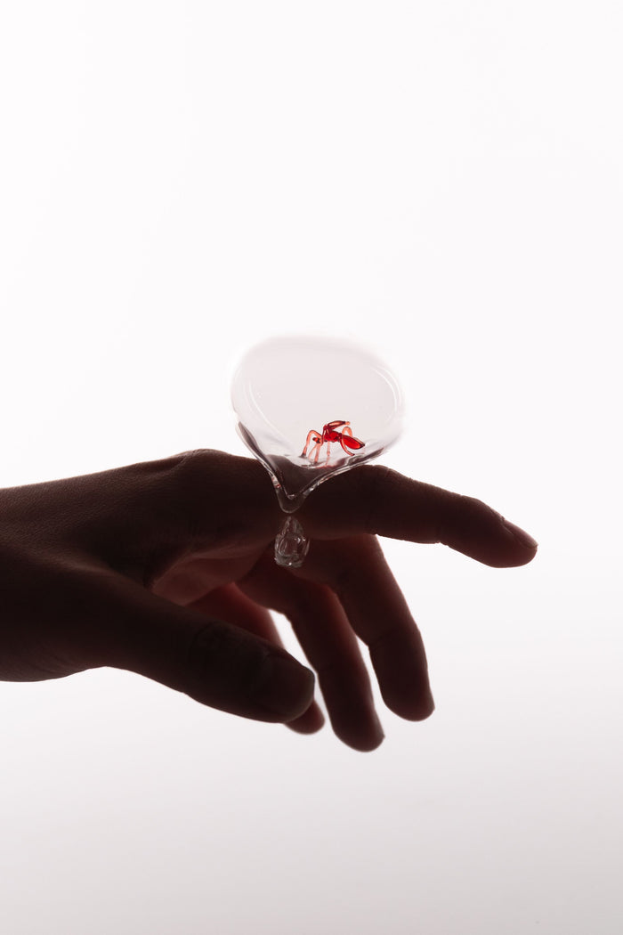 Hand holding a glass object with a small red detail inside