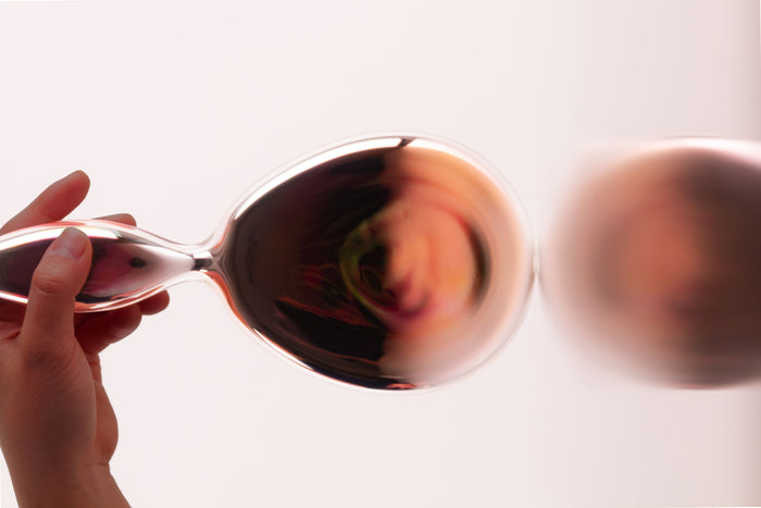 Hand holding a glass object with amber reflections against a white background
