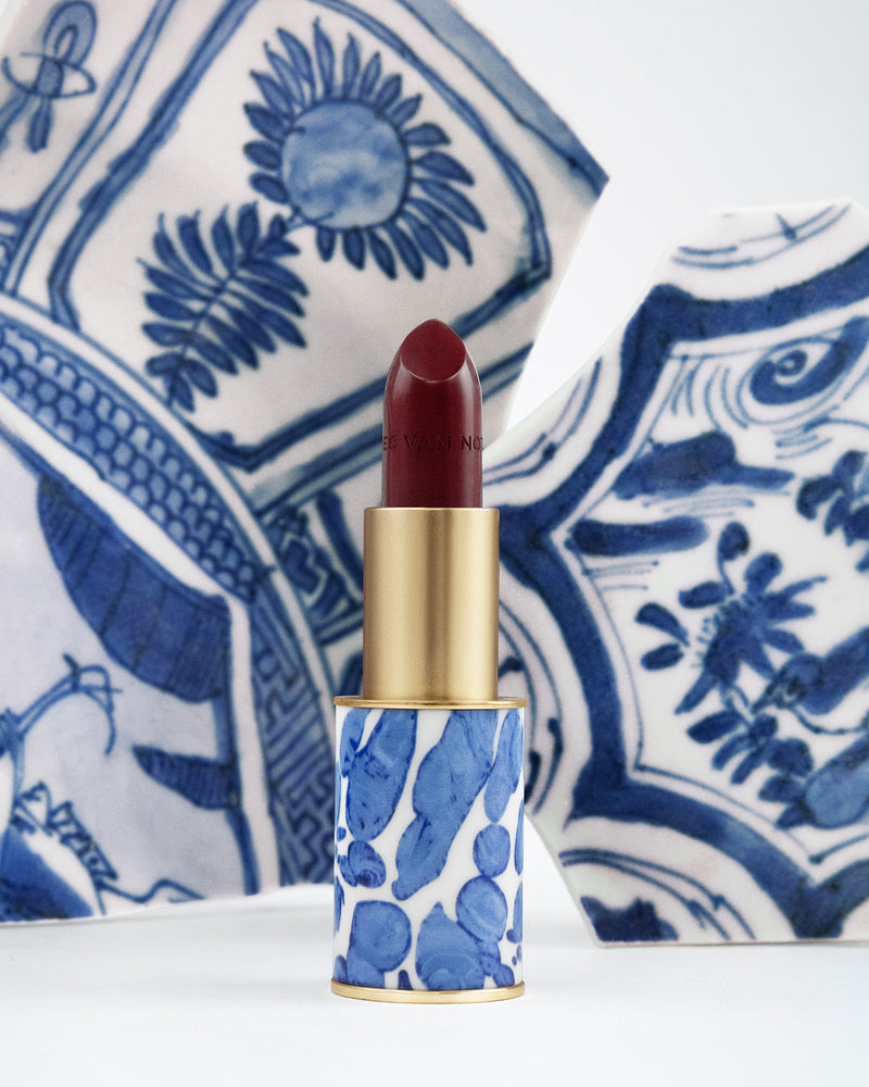 Lipstick with blue and white patterned case against a decorative blue and white background - Dries Van Noten