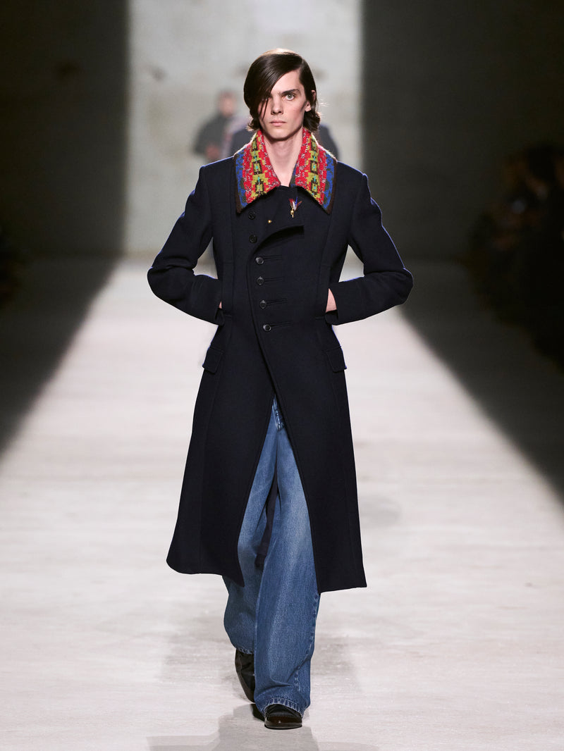 Model walking on a runway wearing a long dark coat with a colorful colar - Dries Van Noten
