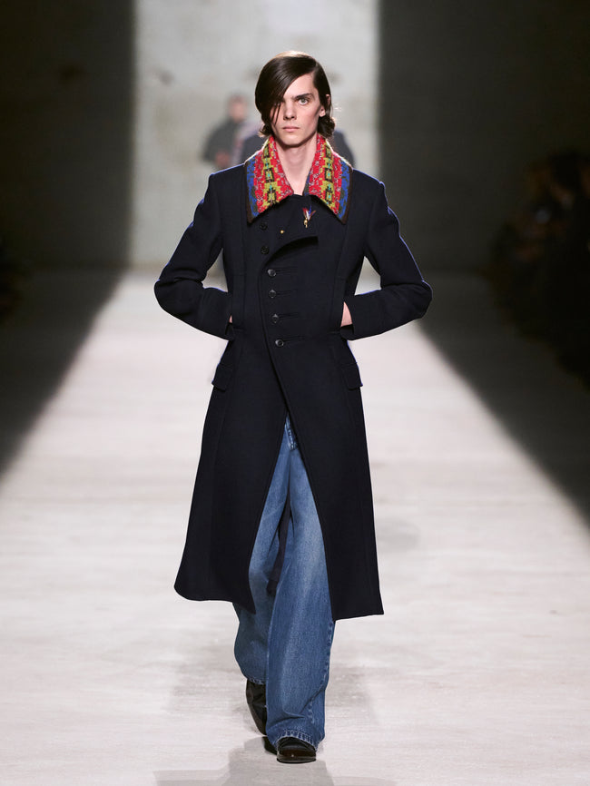 Model walking on a runway wearing a long dark coat with a colorful colar - Dries Van Noten