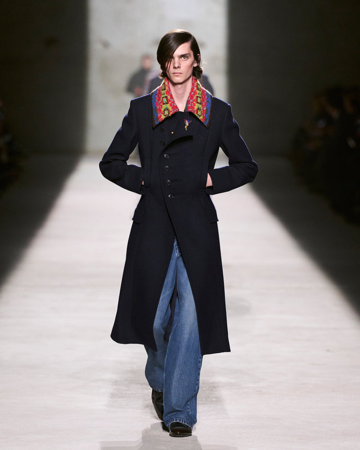 Model walking on a runway wearing a long dark coat with a colorful colar - Dries Van Noten