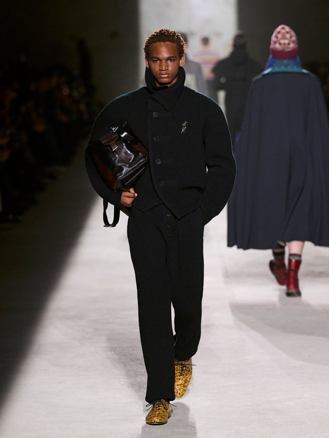 Man walking on a runway wearing a black outfit with a coat and shoes - Dries Van Noten