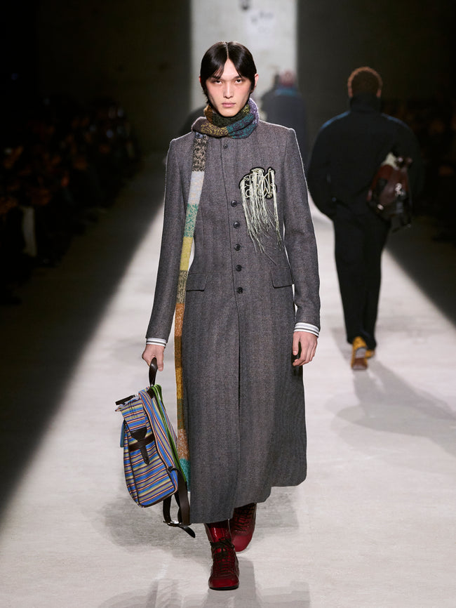 Model walking down a runway wearing a long gray coat with a colorful scarf and bag - Dries Van Noten