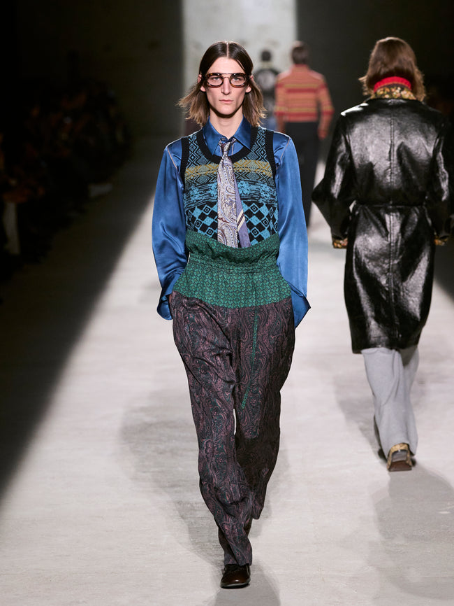 Model walking on a runway wearing a patterned outfit with a blue shirt and green sweater - Dries Van Noten