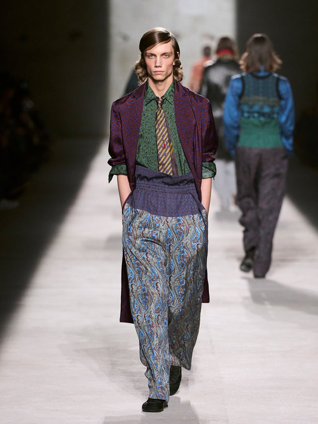 Model walking on a runway wearing a stylish outfit with a patterned coat and pants - Dries Van Noten