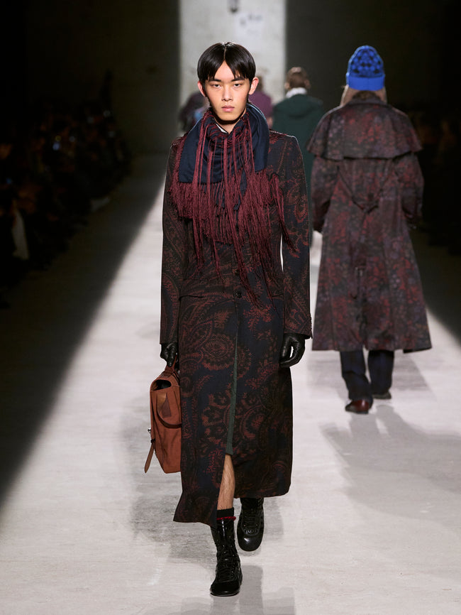 Model walking on a runway wearing a patterned coat and carrying a bag - Dries Van Noten