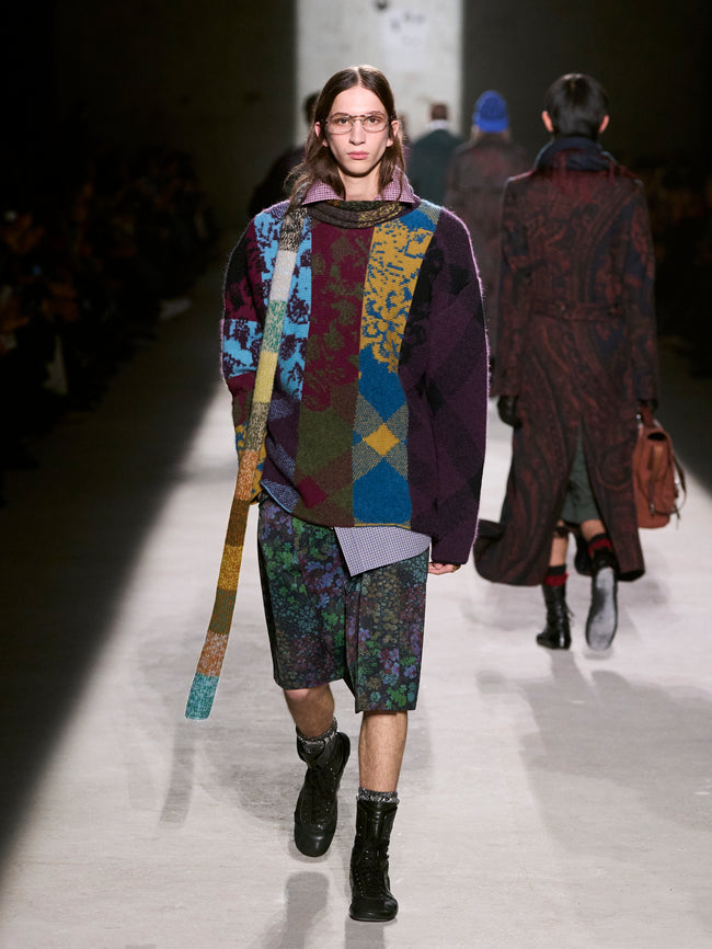 Model walking on a runway wearing a colorful patchwork outfit with a patterned skirt and sweater - Dries Van Noten