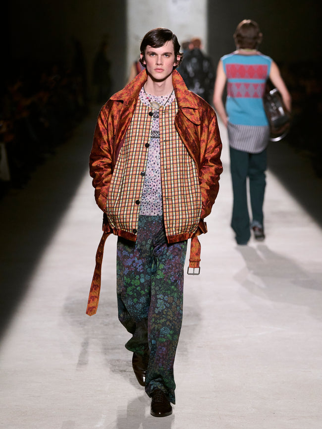 Model walking on a runway wearing a brown jacket and patterned pants - Dries Van Noten
