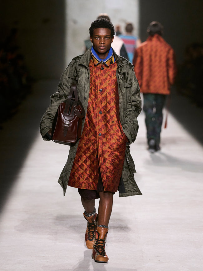 Model walking on a runway wearing a green coat and patterned dress - Dries Van Noten