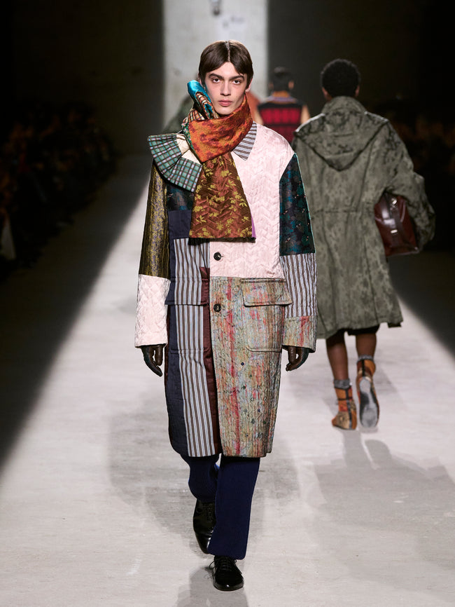 Model walking on a fashion runway wearing a patchwork coat and scarf - Dries Van Noten