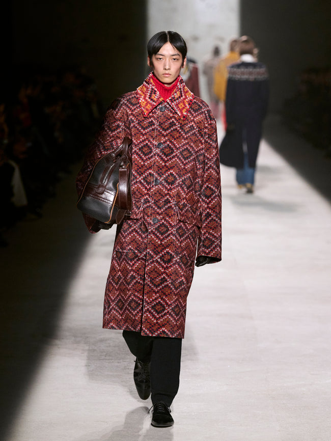 Model walking on a runway wearing a patterned coat and carrying a bag - Dries Van Noten