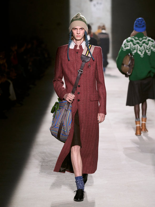 Model walking on a runway wearing a long burgundy coat and colorful beanie - Dries Van Noten