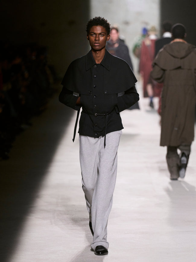 Model walking on a runway wearing a black jacket and light gray pants - Dries Van Noten