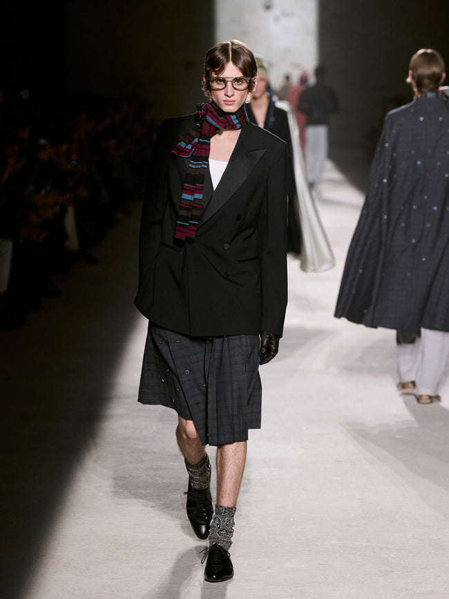 Model walking on a runway wearing a black coat and plaid scarf - Dries Van Noten