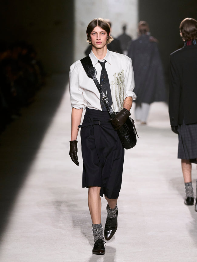 Model walking on a runway wearing a white shirt, black suspenders, and dark pants - Dries Van Noten