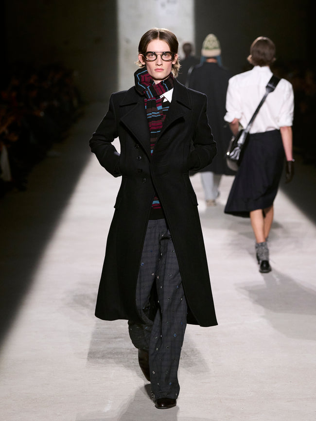 Model walking on a runway wearing a long black coat and glasses - Dries Van Noten