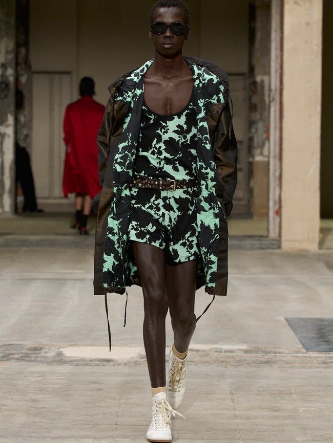 Model wearing a green and black camouflage outfit with sunglasses on a runway. - Dries Van Noten