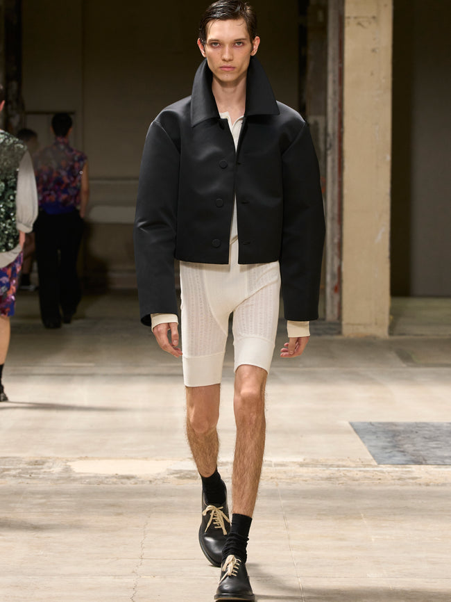 Model walking on a runway wearing a black jacket and white pants. - Dries Van Noten