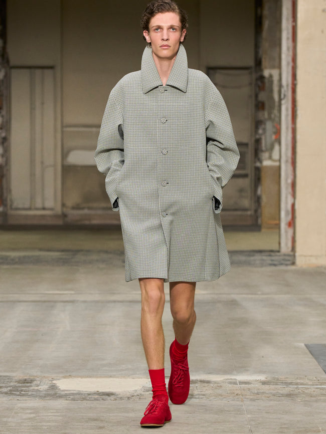 Man wearing a gray coat and red shoes standing in an open doorway. - Dries Van Noten