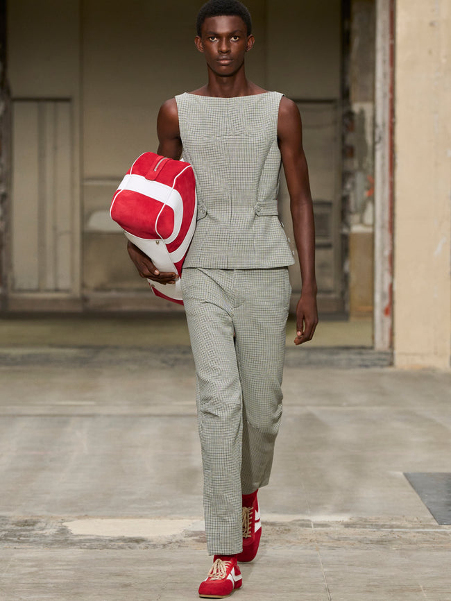 Model walking on a runway wearing a sleeveless top and pants with a red and white bag. - Dries Van Noten
