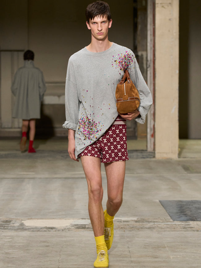 Model walking on a runway wearing a gray sweater with floral patterns and maroon shorts. - Dries Van Noten