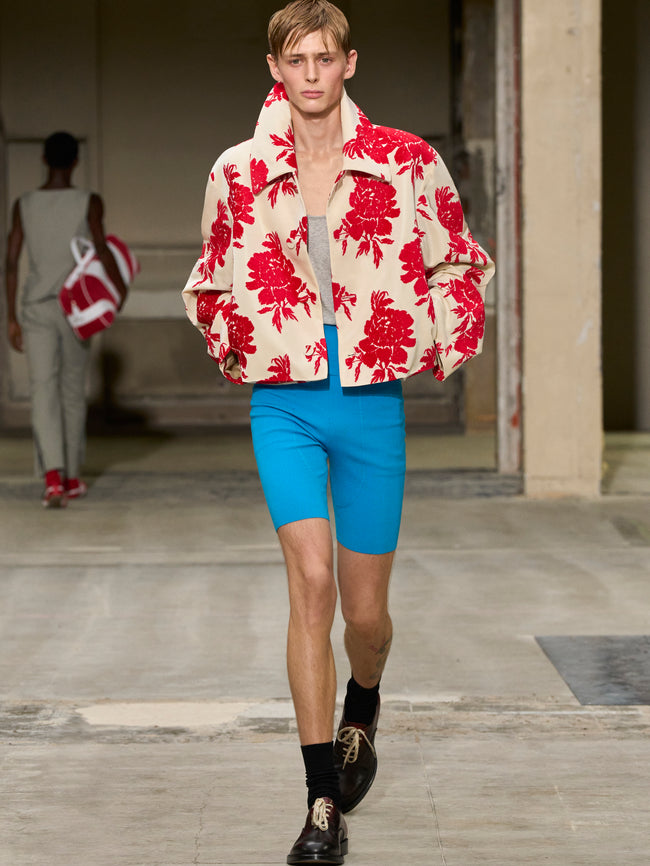 Model walking on a runway wearing a red and white floral jacket with blue shorts. - Dries Van Noten