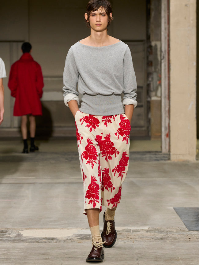 Model walking on a runway wearing a gray sweater and red floral pants. - Dries Van Noten