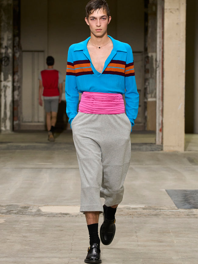 Model walking on a runway wearing a colorful striped shirt and gray pants. - Dries Van Noten