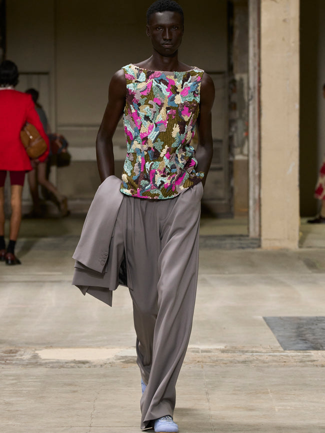 Model wearing a colorful floral top and gray pants on a runway. - Dries Van Noten