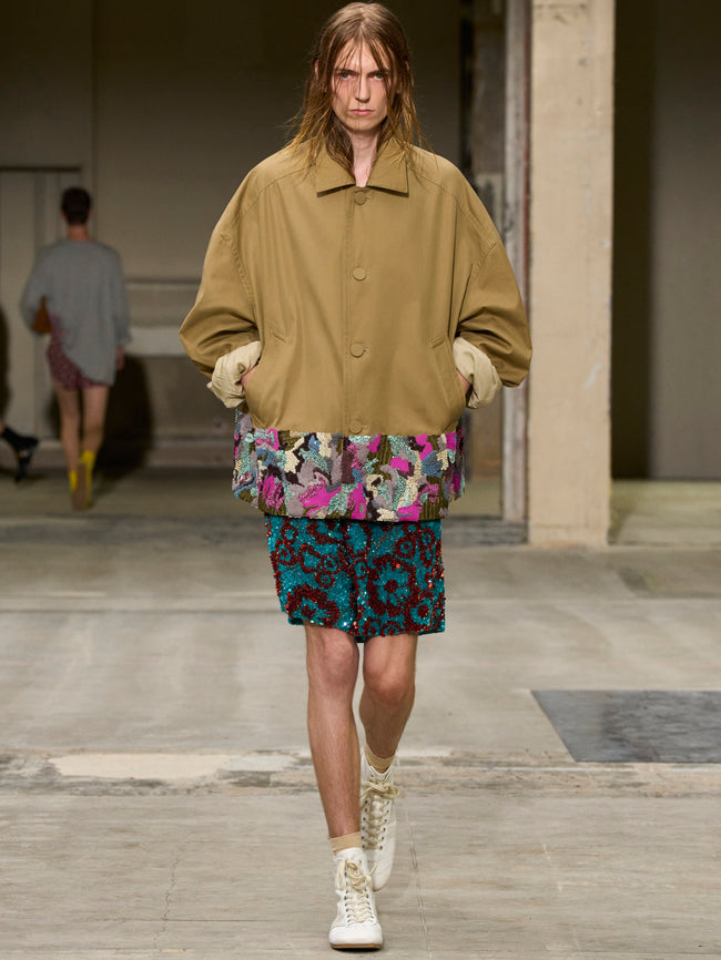 Model walking on a runway wearing a beige jacket and patterned skirt. - Dries Van Noten
