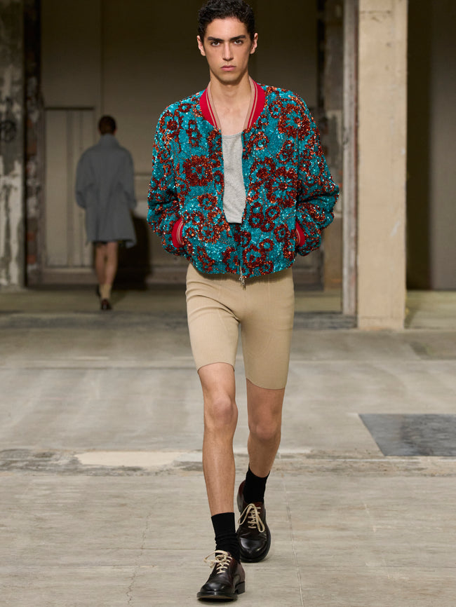 Model wearing a patterned jacket and beige shorts on a runway. - Dries Van Noten