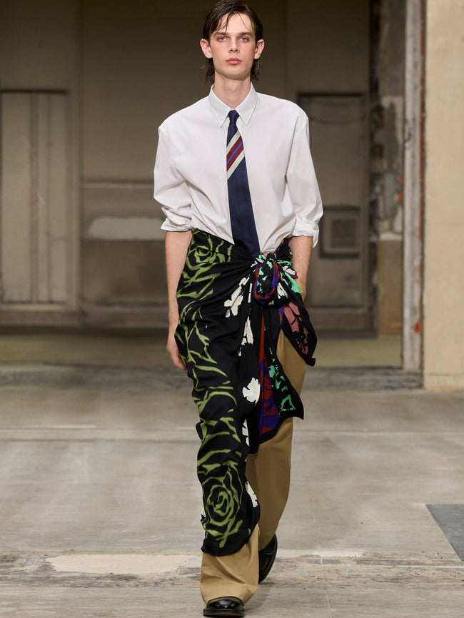 Model wearing a white shirt, patterned tie, and colorful pants on a runway. - Dries Van Noten