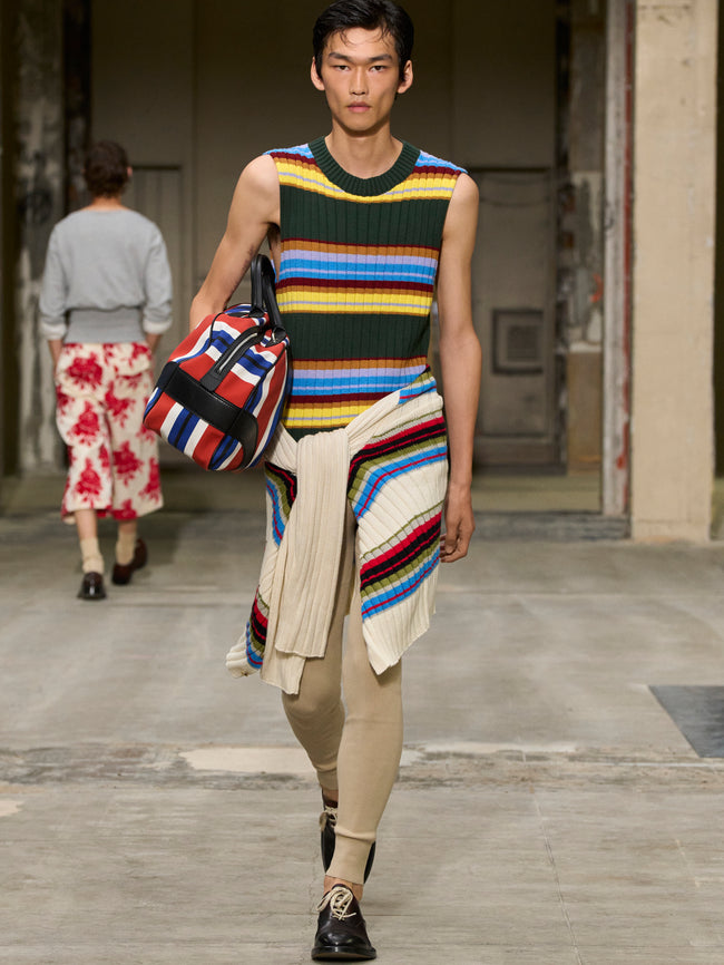 Model walking on a runway wearing a colorful striped sleeveless top and beige pants. - Dries Van Noten