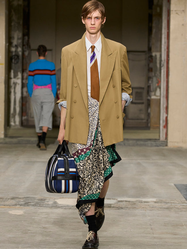 Model walking on a runway wearing a stylish outfit with a beige coat and patterned skirt. - Dries Van Noten