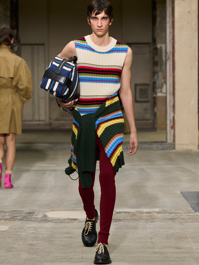 Model walking on a runway wearing a colorful outfit with a striped top and maroon pants. - Dries Van Noten