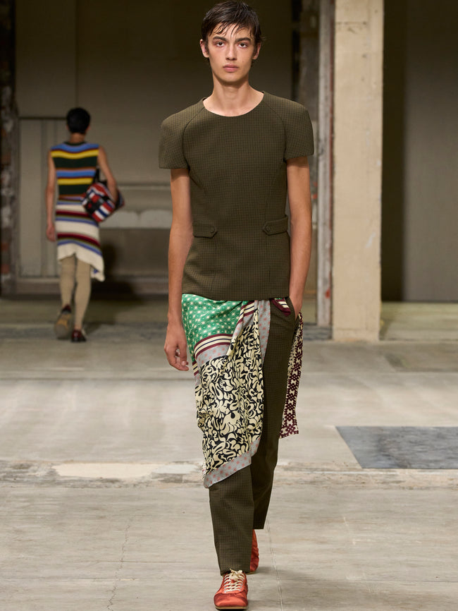 Model walking on a runway wearing a green outfit with a patterned scarf. - Dries Van Noten