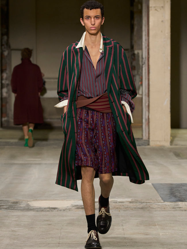 Model walking on a runway wearing a striped outfit with a long coat. - Dries Van Noten