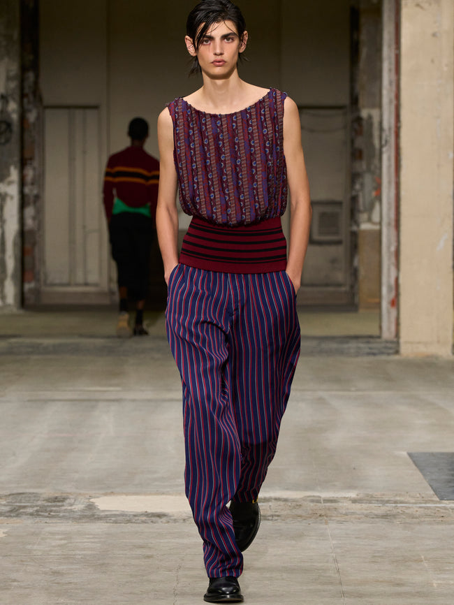 Model walking on a runway wearing a patterned top and striped pants. - Dries Van Noten
