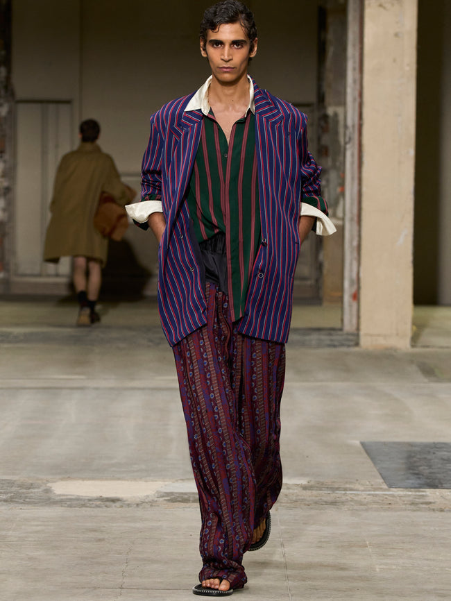 Model walking on a runway wearing a purple striped suit with a white shirt. - Dries Van Noten