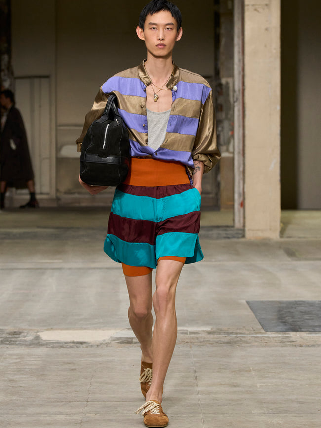 Model walking on a runway wearing a colorful outfit with a striped skirt and backpack. - Dries Van Noten