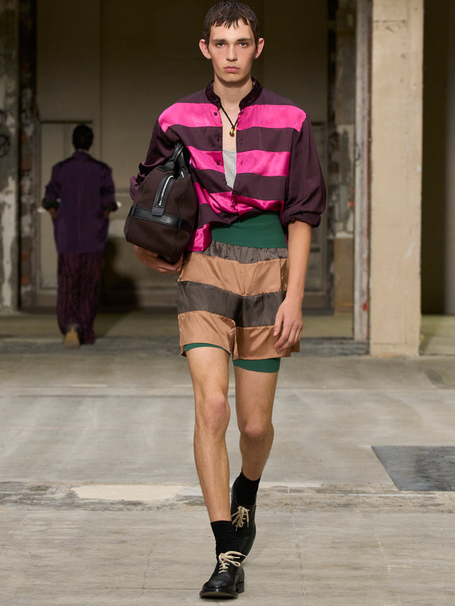 Model walking on a runway wearing a colorful striped shirt and patterned shorts. - Dries Van Noten