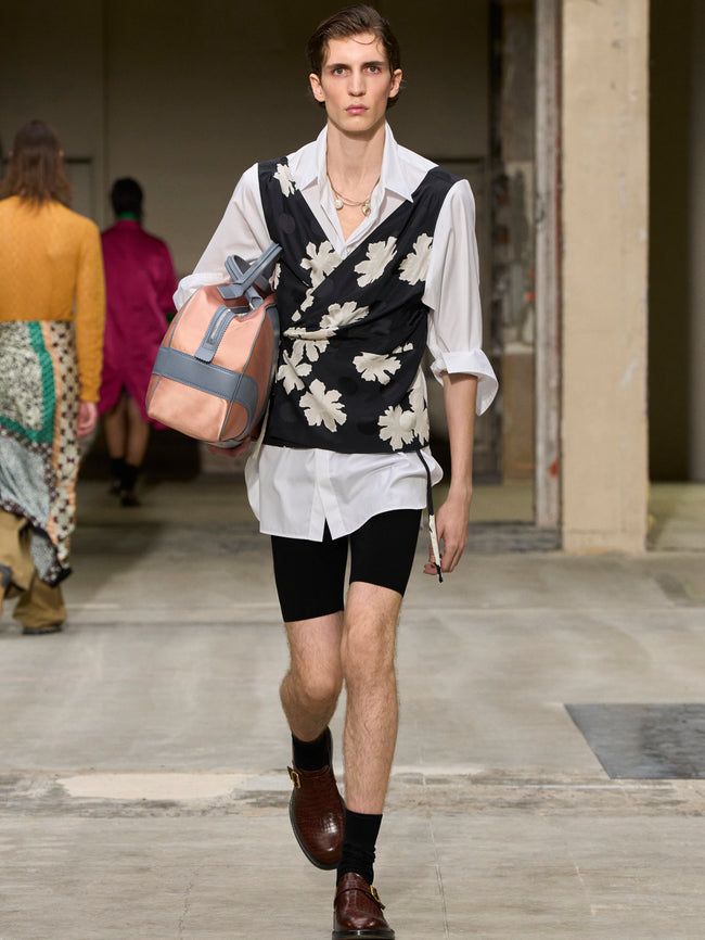Model walking on a runway wearing a floral vest and white shirt with black shorts. - Dries Van Noten