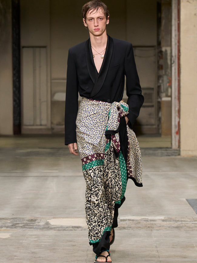 Model walking on a runway wearing a black jacket and patterned pants. - Dries Van Noten