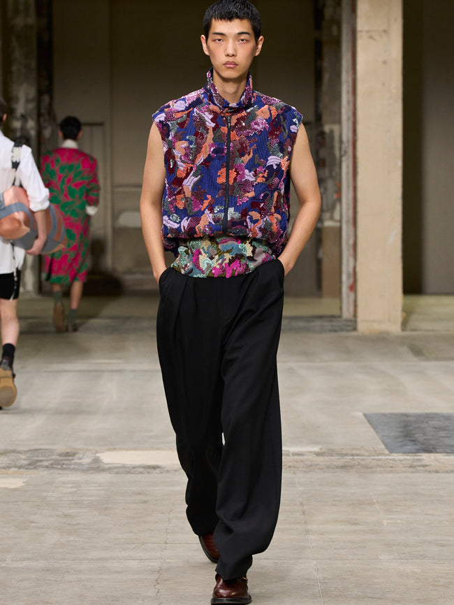 Model walking on a runway wearing a colorful floral shirt and black pants. - Dries Van Noten