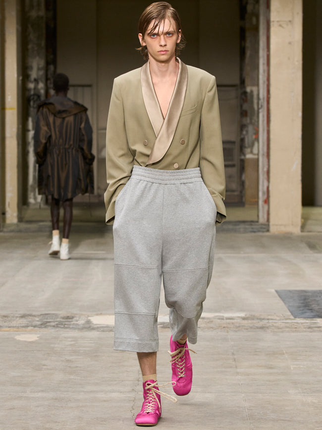 Model wearing a green blazer, gray pants, and pink shoes in an urban setting. - Dries Van Noten